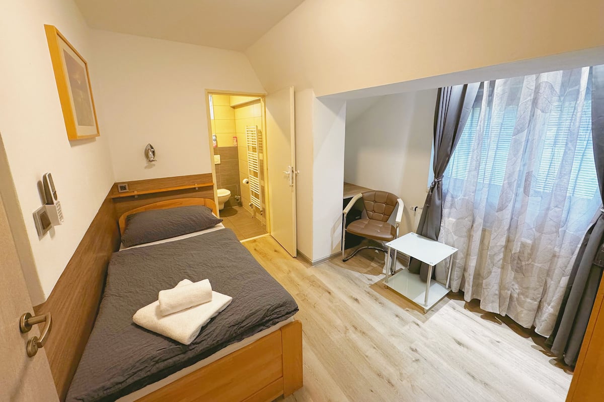 Une chambre avec deux lits, un petit bureau et une chaise. On peut apercevoir la salle de bain à travers une porte ouverte.