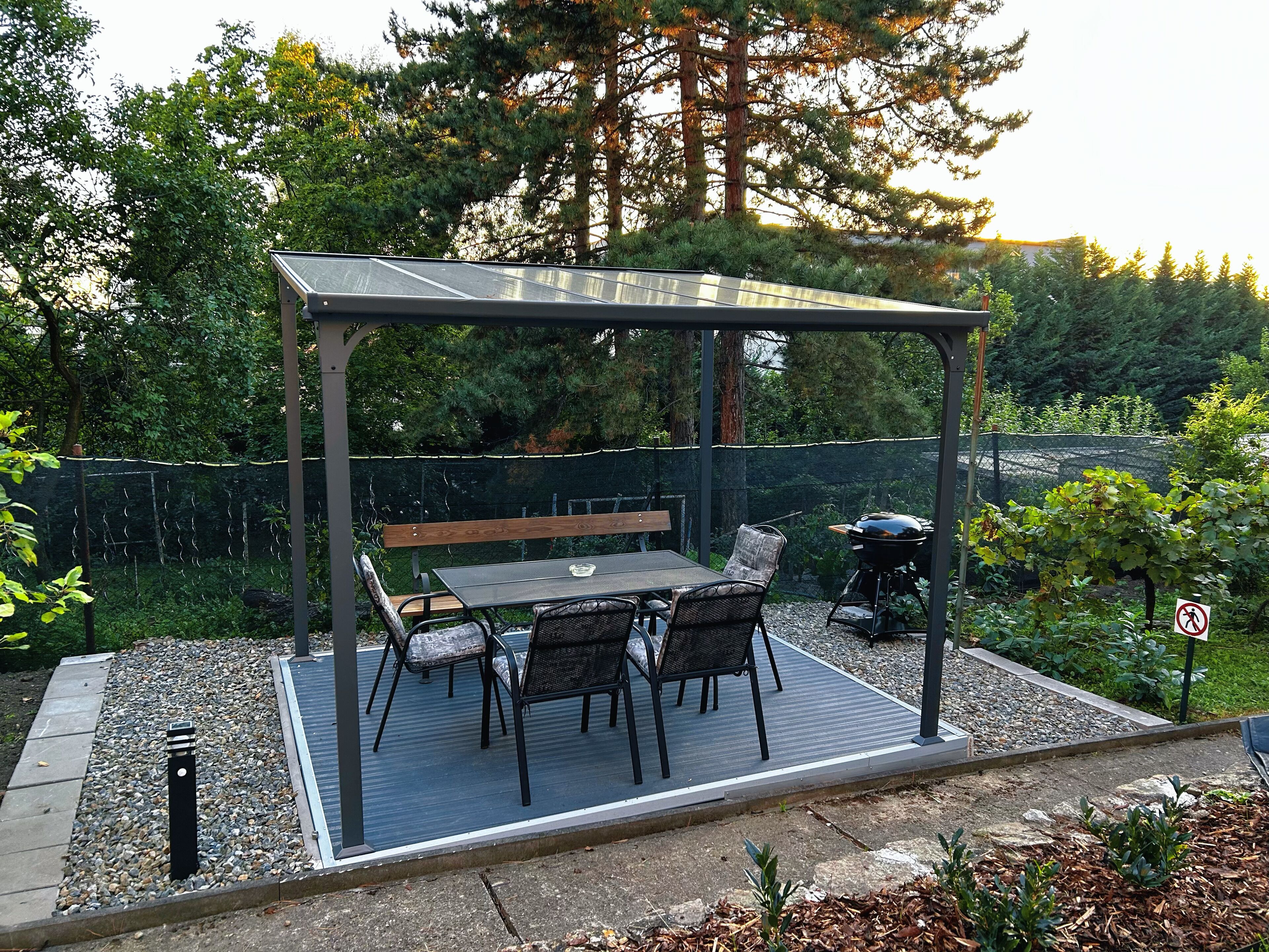 An outdoor patio with a pergola, a table, chairs, and a grill.