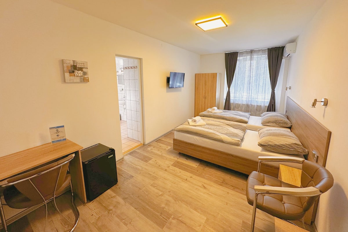 Une chambre à coucher avec un lit, un bureau, une chaise, une télévision et une fenêtre avec des rideaux.