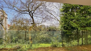 Un jardin clos, agrémenté de diverses plantes et arbres, avec un bâtiment en arrière-plan et un ciel dégagé.