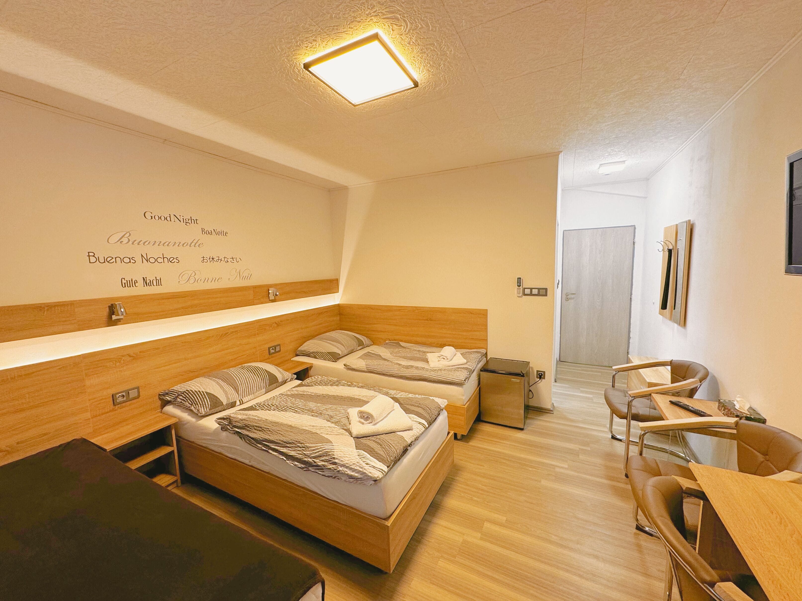 Une chambre d’hôtel avec deux lits, un bureau et une chaise. Il y a un miroir sur le mur et une porte qui donne sur une autre pièce.