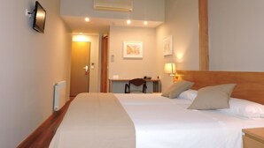 A hotel room with two beds, a wooden headboard, a desk with a chair, and a wall-mounted air conditioner. - El Nogal (Valladolid)