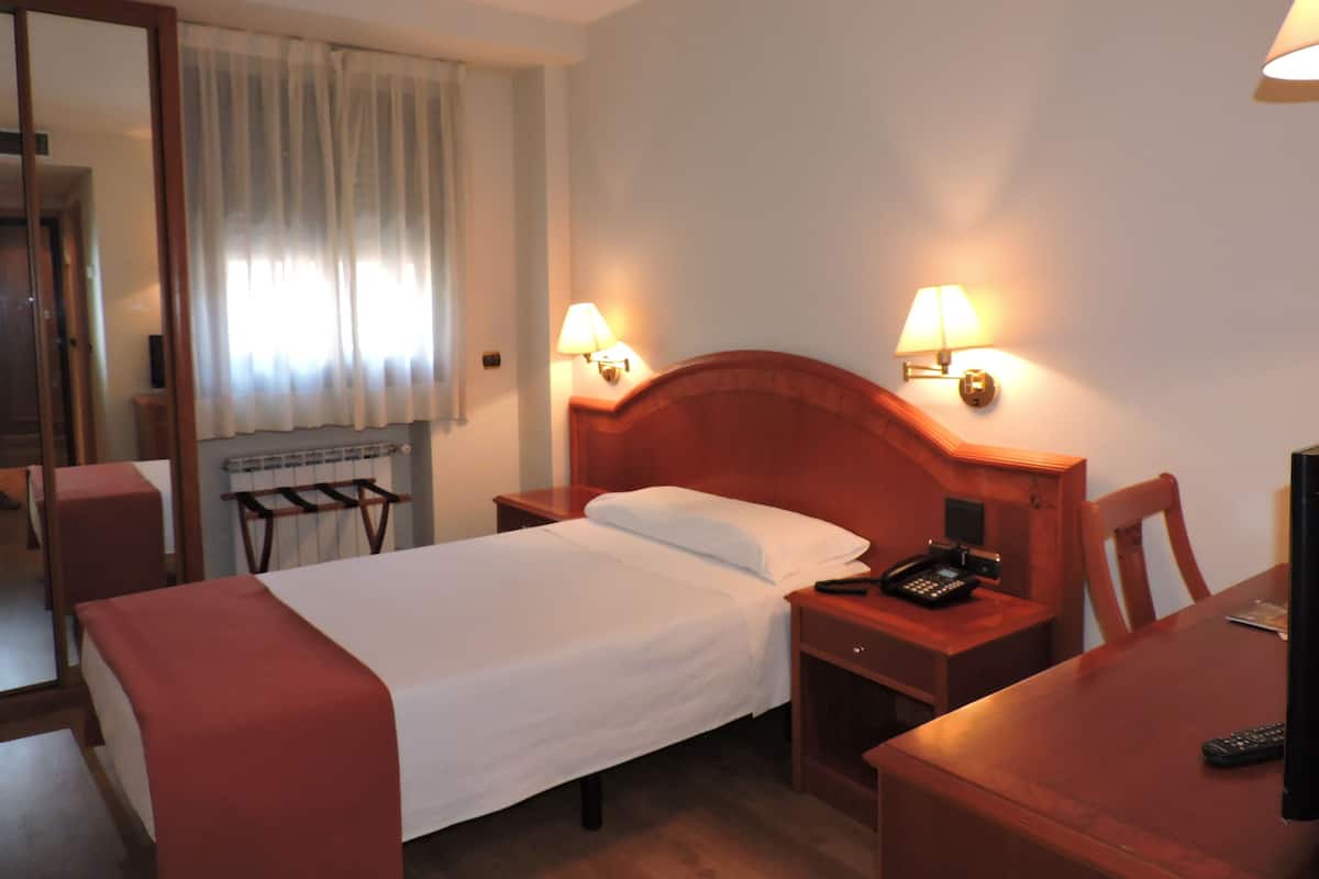 Een hotelkamer met een bed, nachtkastjes, een bureau, een stoel, een lamp en een telefoon.