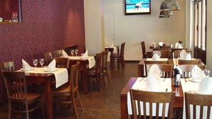 A restaurant interior with wooden tables and chairs, white tablecloths, and a television mounted on the wall. - El Nogal (Valladolid)