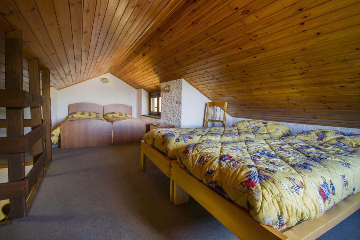 A bedroom with a wooden ceiling, a bed with a floral duvet, and a wooden bench.
