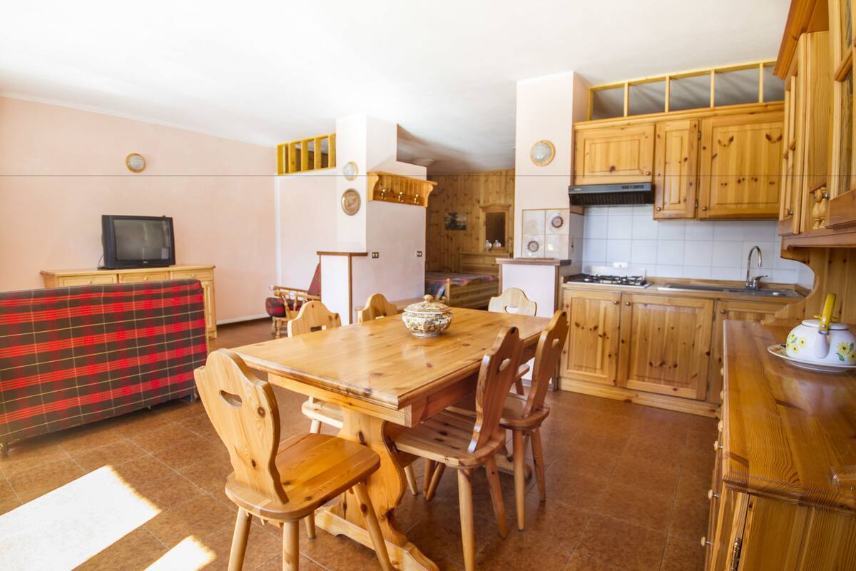 A cozy kitchen with wooden cabinets, a dining table with chairs, and a television on a stand.
