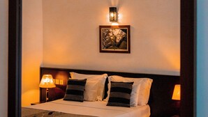 A neatly made bed with a headboard, two bedside lamps, and a wall-mounted light fixture. - Riverside Inn Fuji (Bentota)