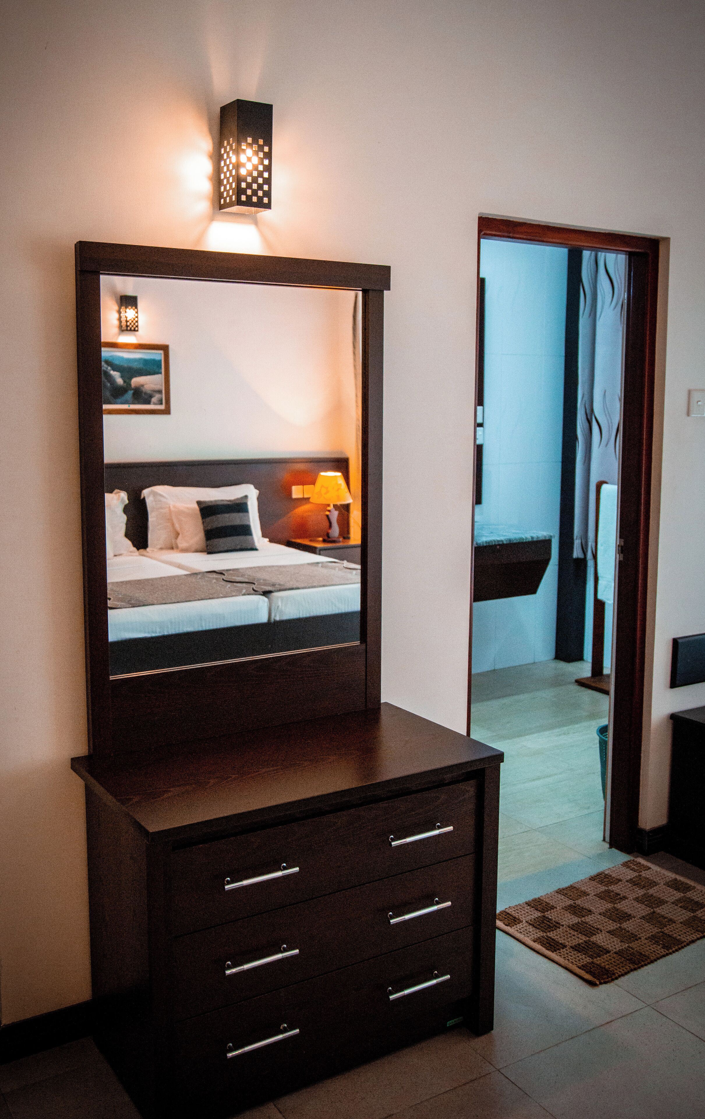 A hotel room with a bed, bedside table, lamp, and a dresser with drawers.