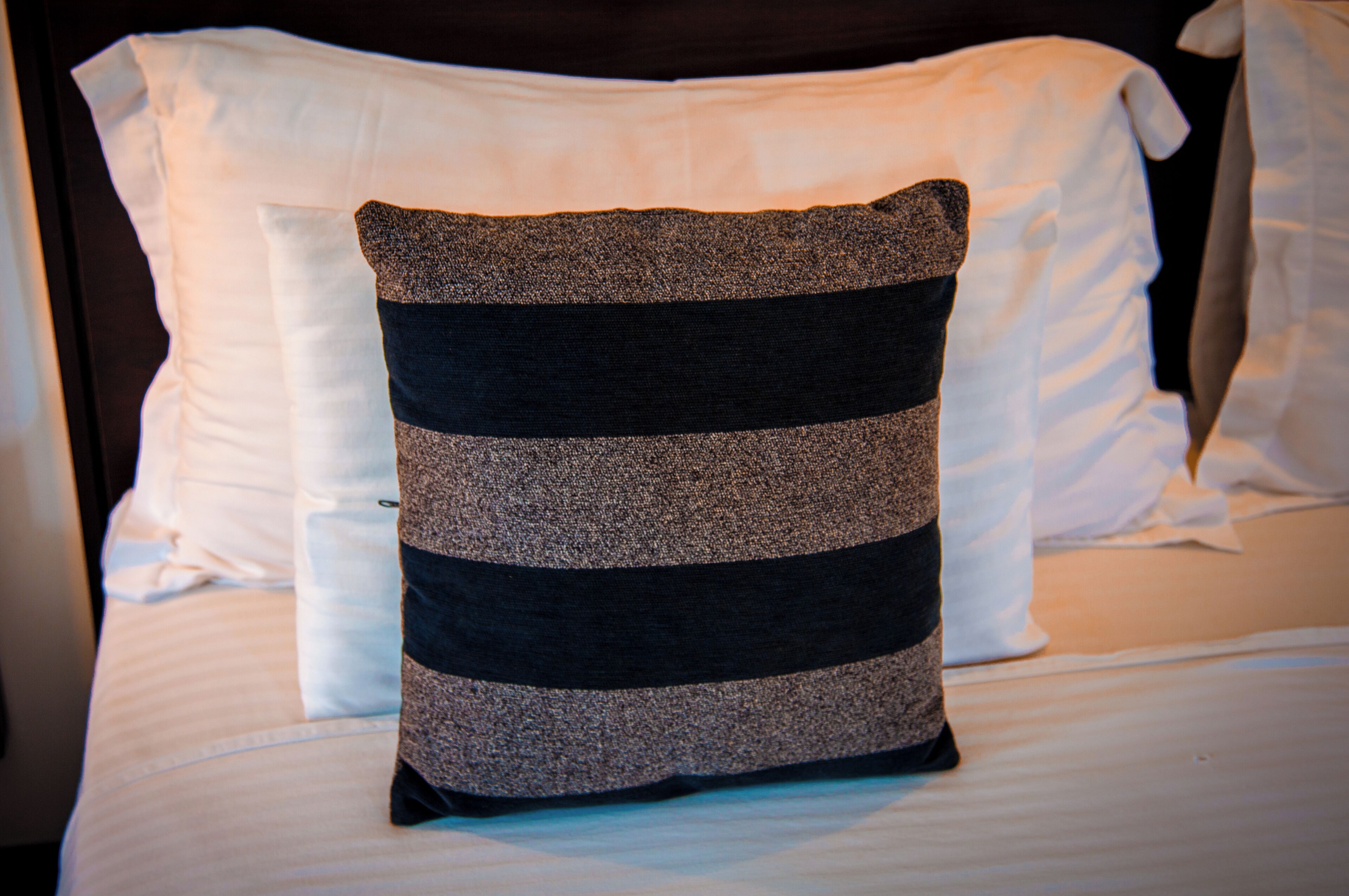 A bed with white pillows and a striped pillow.