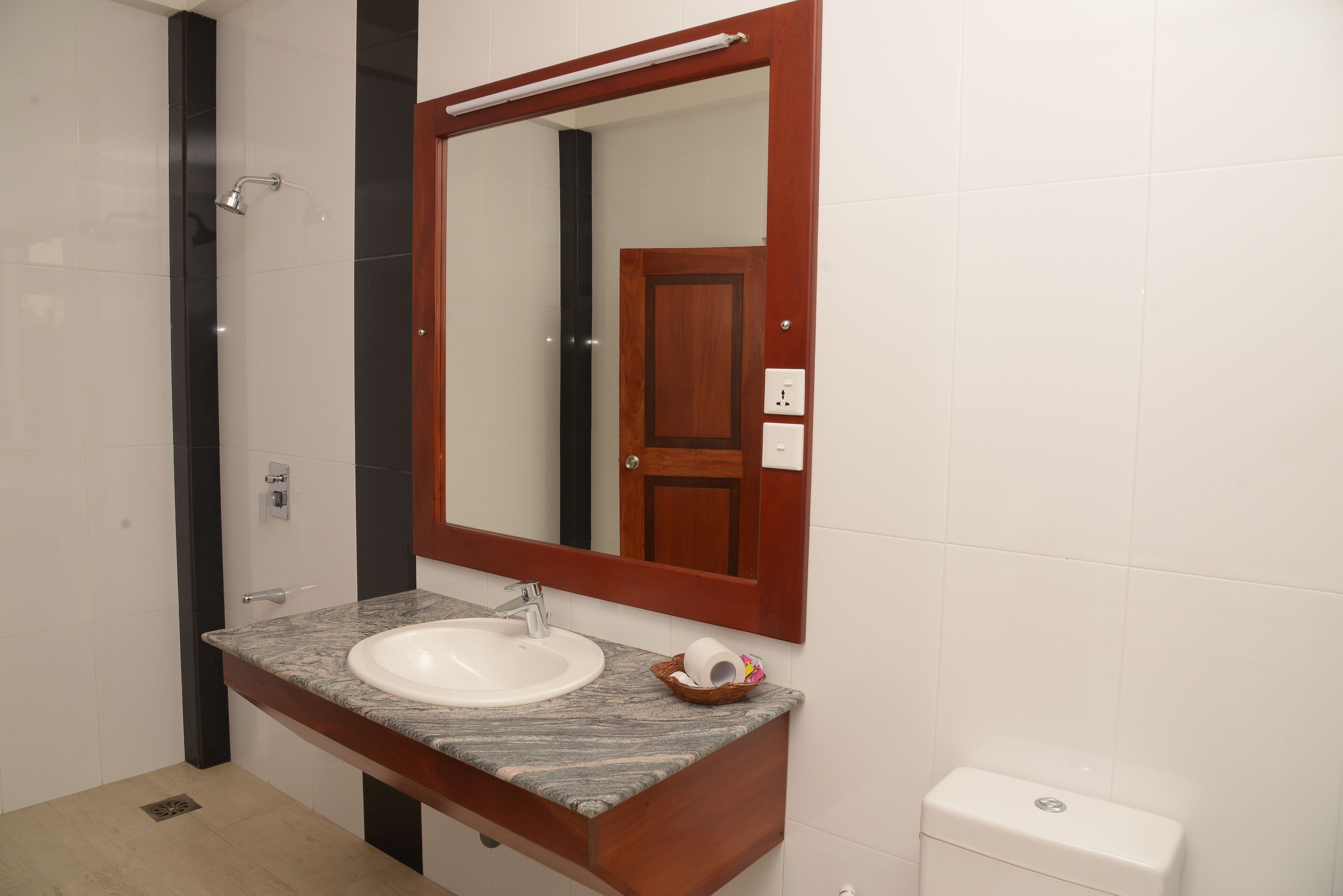 A bathroom with a white sink, a wooden vanity, a mirror, and a toilet.