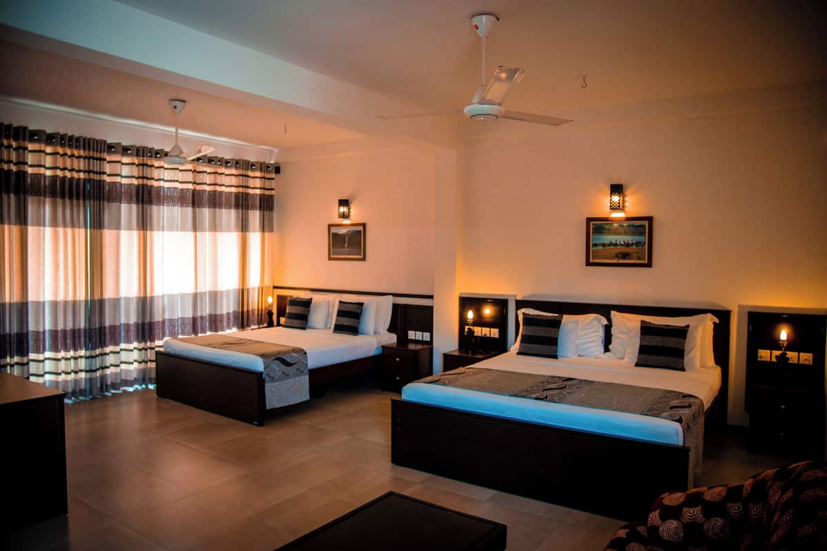 A hotel room with two beds, a desk, and a ceiling fan.