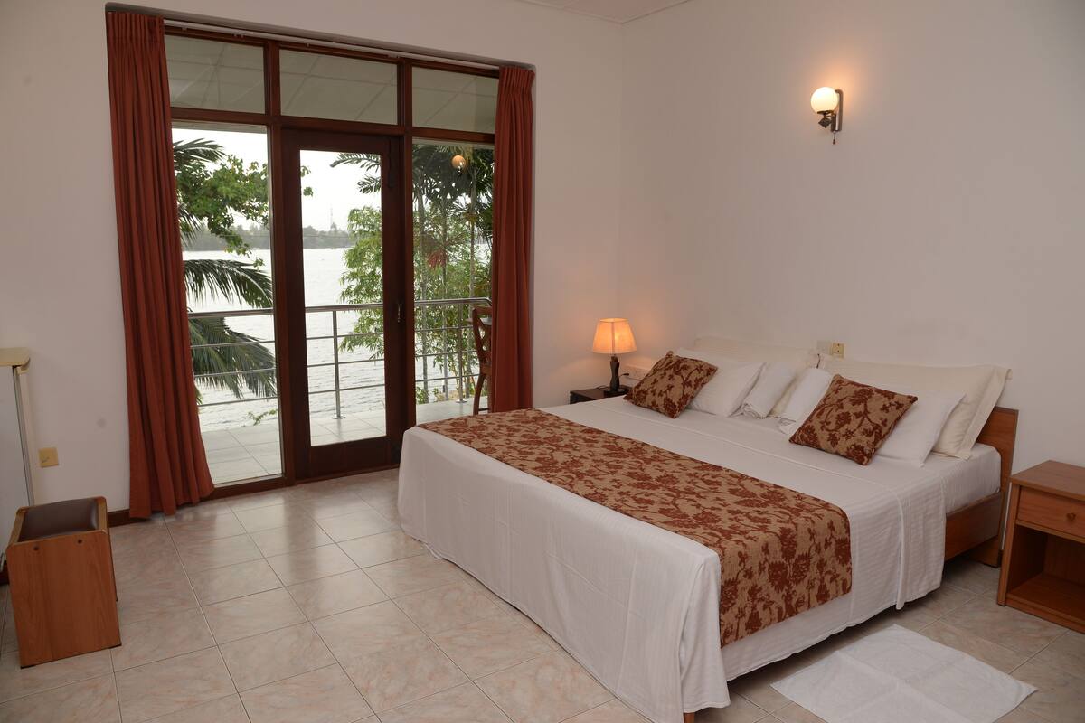 A hotel room with a large bed, a nightstand, a lamp, and a view of the outdoors through a sliding door.