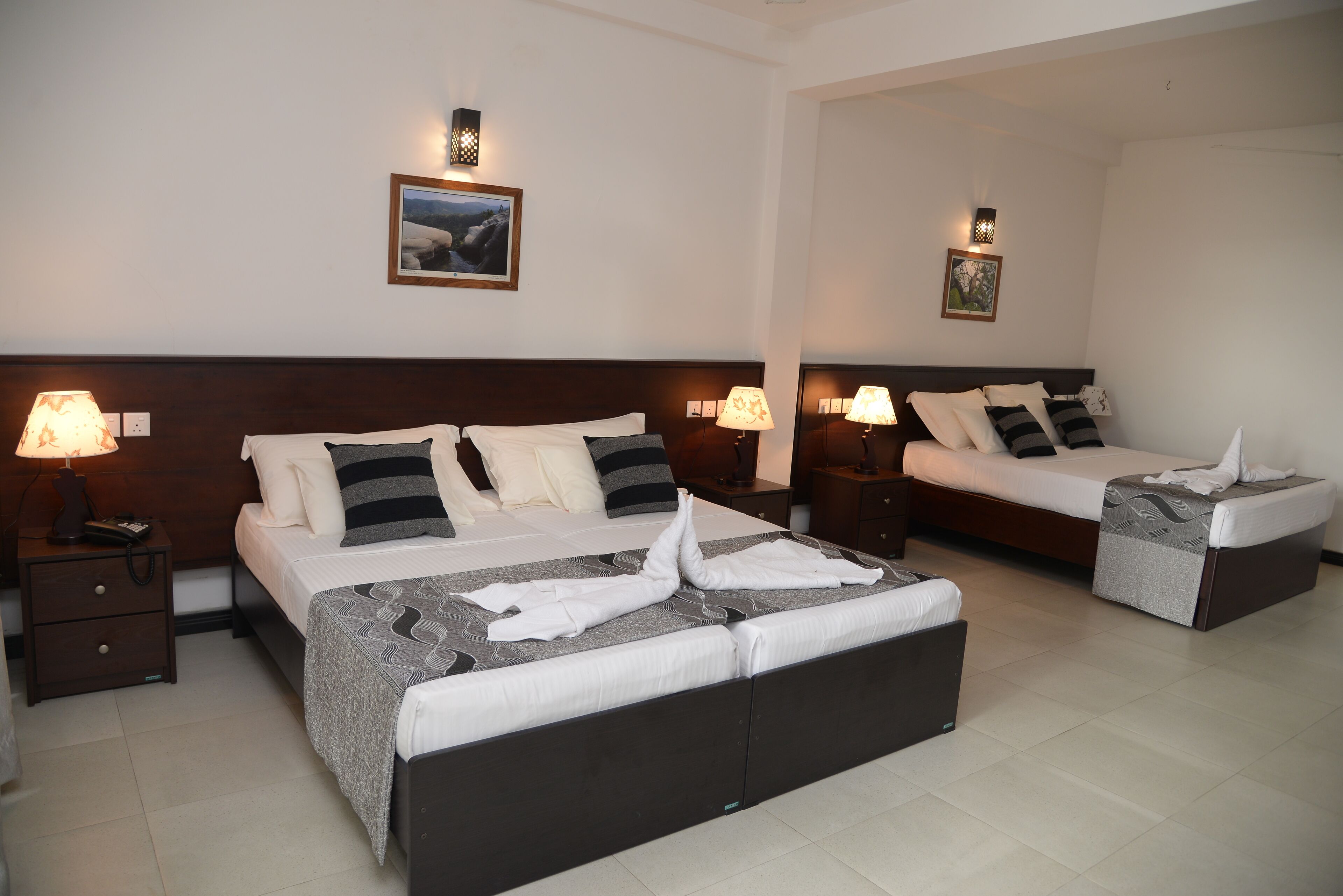A hotel room with two beds, each with a headboard, bedside tables, lamps, and a framed picture on the wall.