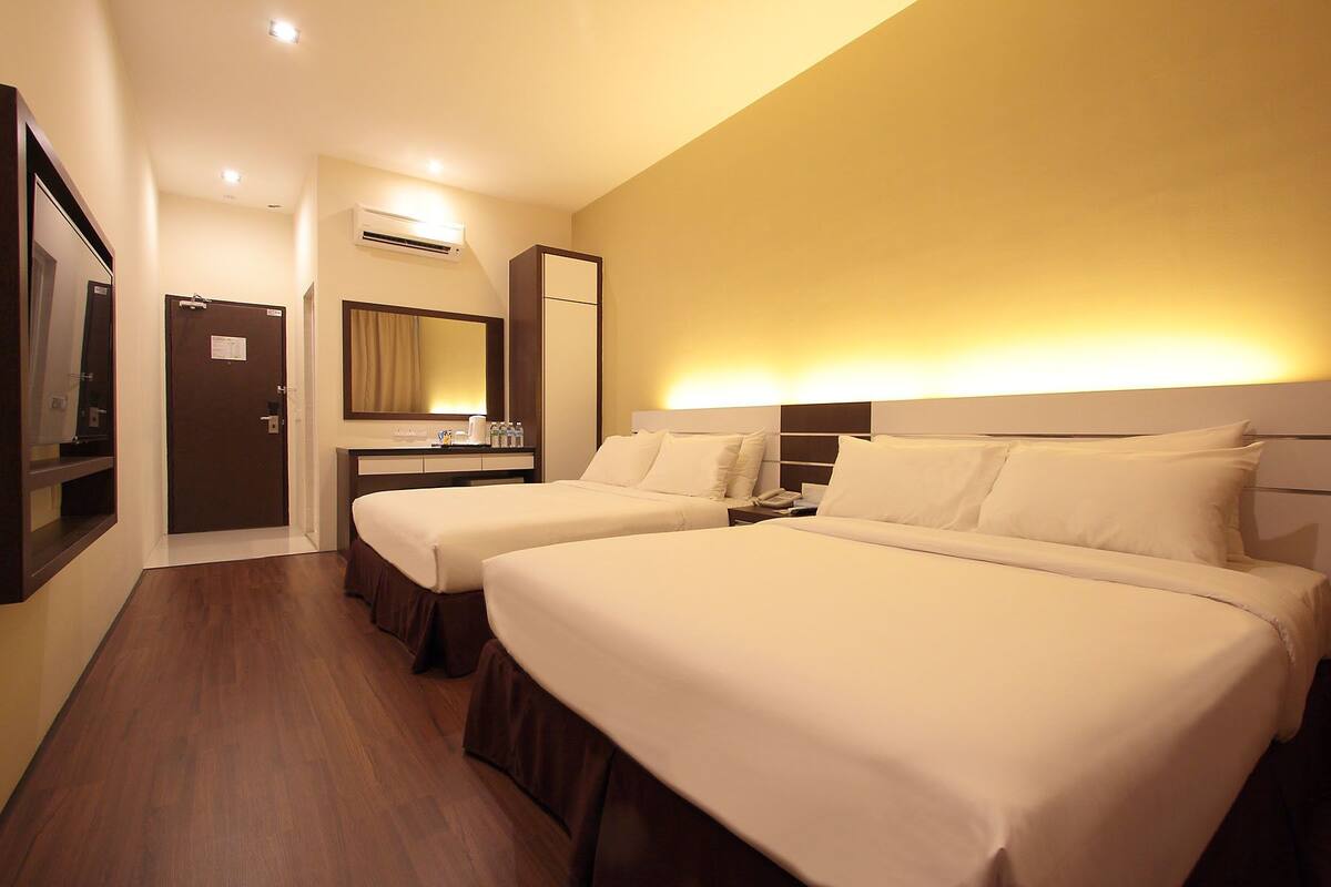 A hotel room with two beds, a desk, a mirror, and an air conditioning unit.