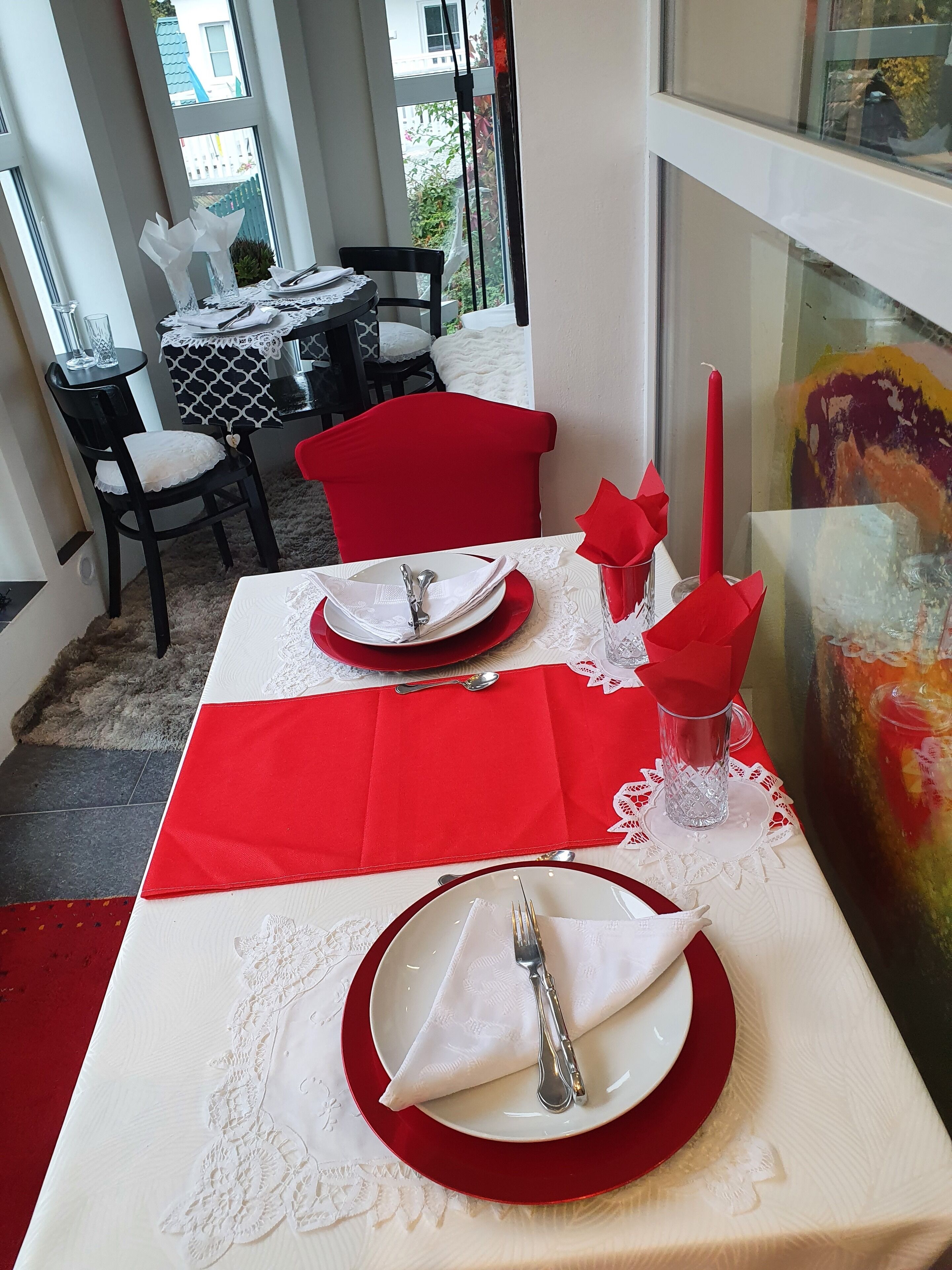 Zona de menjador amb una taula preparada per a dues persones, amb serretes vermelles, plats blancs i coberteria.