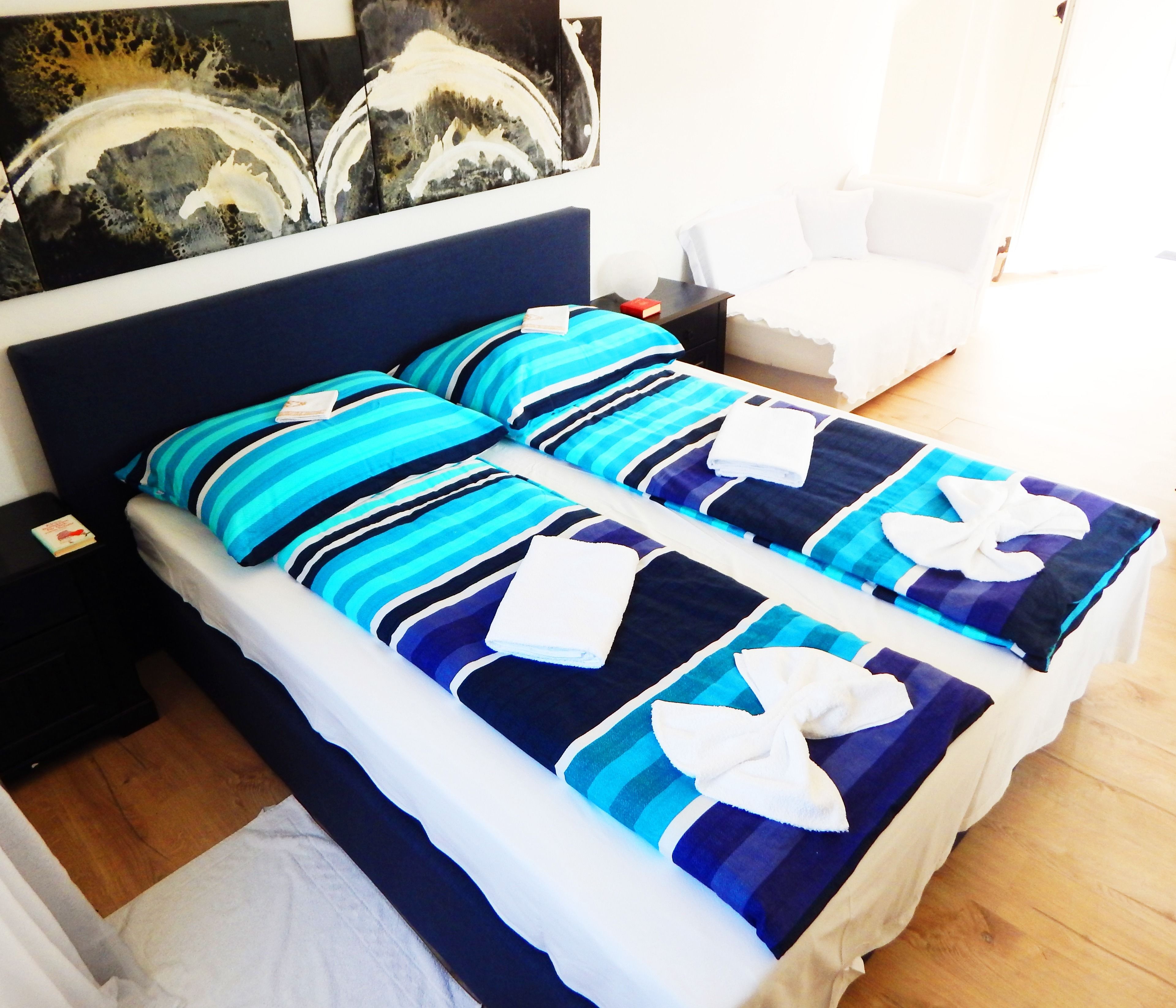 Camera d'albergo con un letto grande, biancheria a righe, un comodino, una sedia e un quadro appeso al muro.