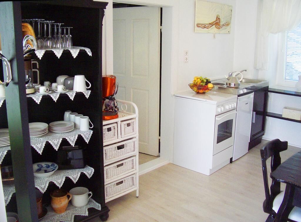 Cocina compacta con electrodomésticos blancos, un pequeño comedor y un estante decorativo con cristalería y vajilla.