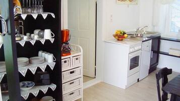 Cocina compacta con electrodomésticos blancos, un pequeño comedor y un estante decorativo con cristalería y vajilla.