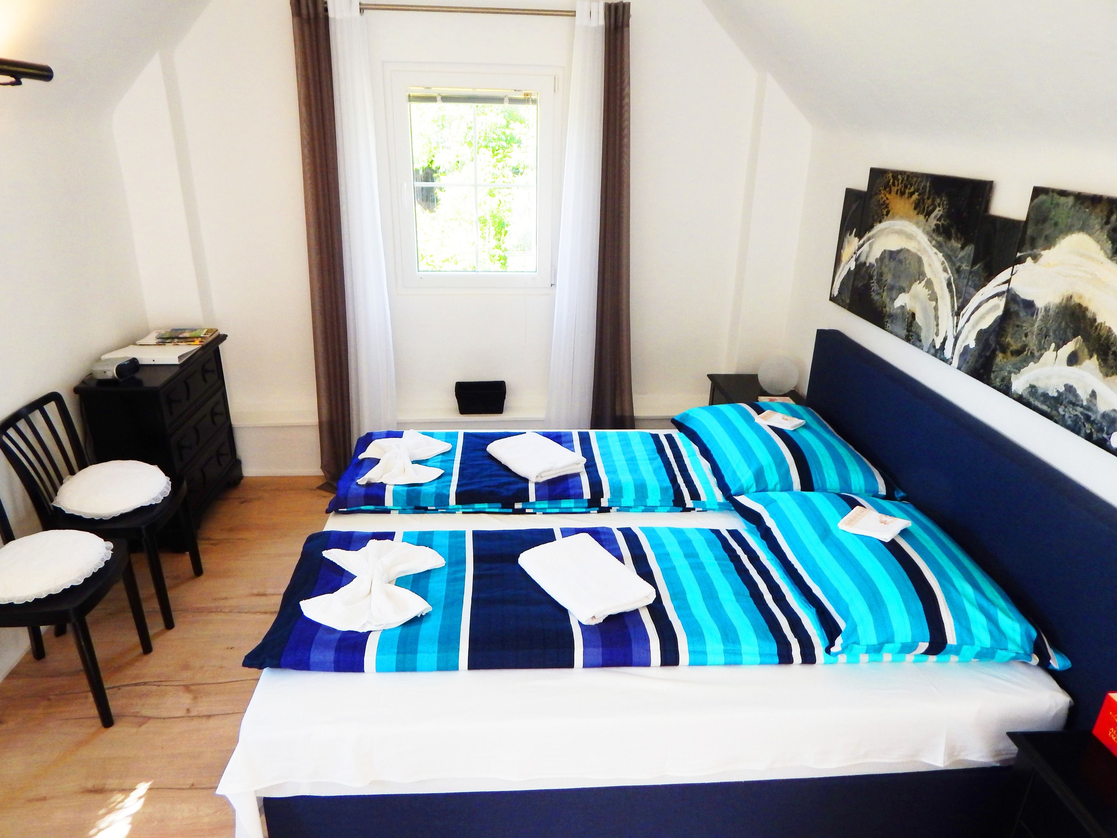 Ein Schlafzimmer mit einem Bett, zwei Stühlen, einer Kommode und einem Fenster mit Vorhängen.