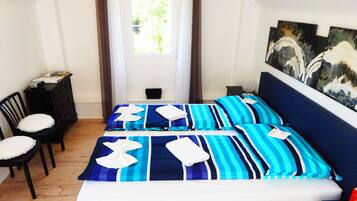 Ein Schlafzimmer mit einem Bett, zwei Stühlen, einer Kommode und einem Fenster mit Vorhängen.