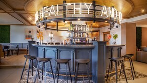 Zona de bar con un letrero de neón que dice "HEALTHY AND", taburetes y una variedad de botellas y vasos en estantes.