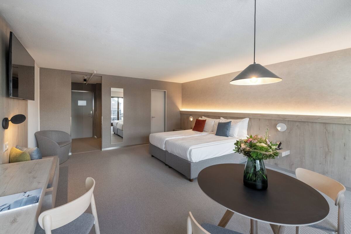 A modern hotel room with a bed, bedside table, and a dining area with a table and chairs.