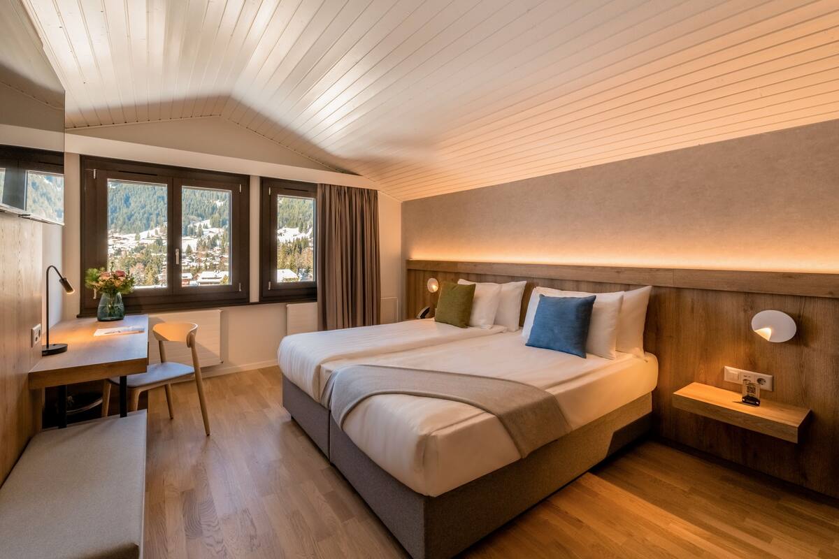 A modern hotel room with a large bed, a desk, and a view of the mountains.