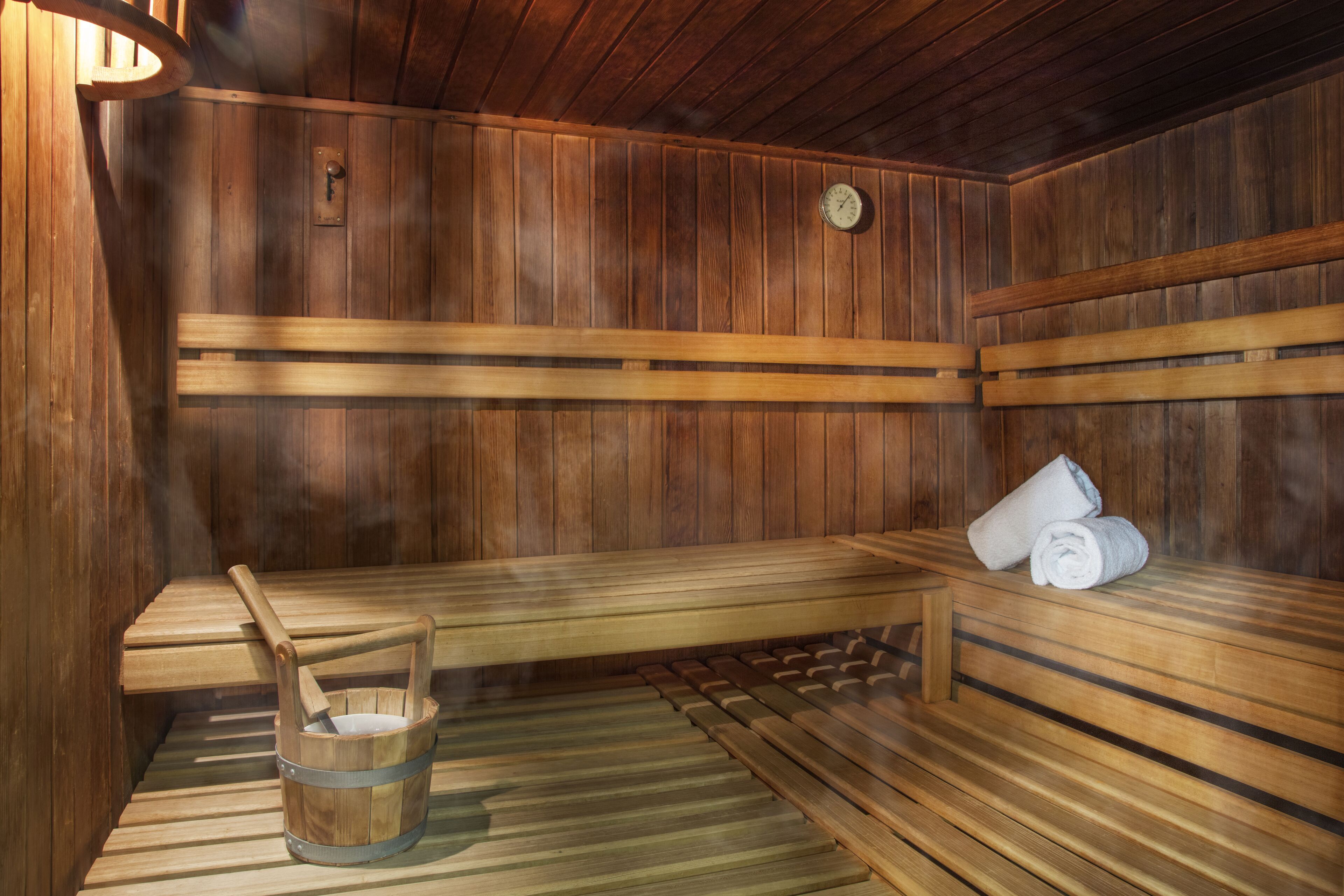 Un sauna avec des bancs en bois, un seau en bois et une serviette posée sur l’un des bancs.