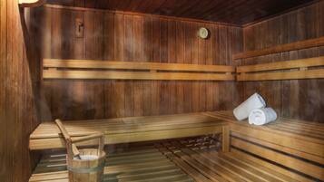 Un sauna avec des bancs en bois, un seau en bois et une serviette posée sur l’un des bancs.