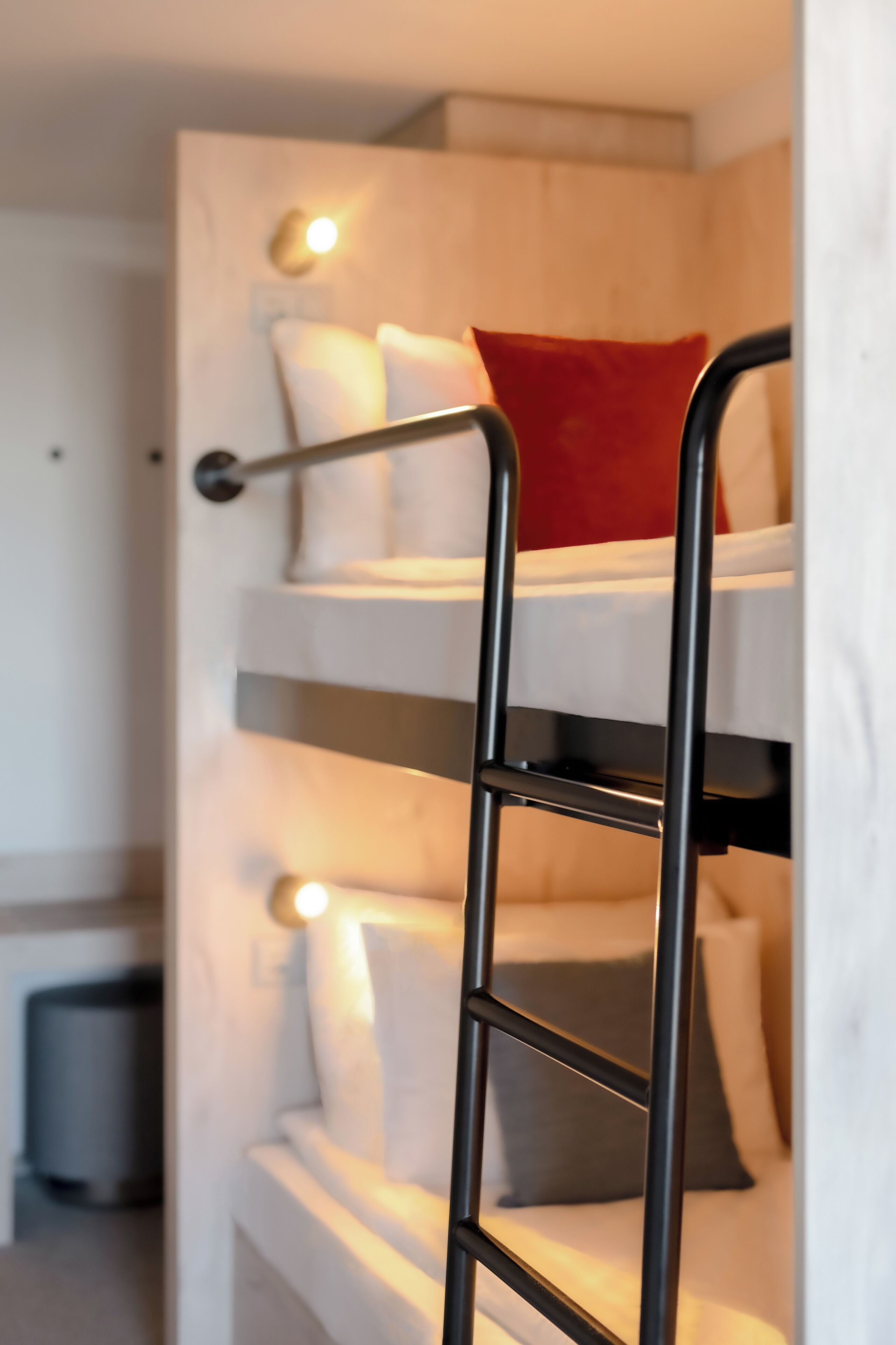 Ein Stockbett mit einer Leiter, weißer Bettwäsche und einem roten Kopfkissen.
