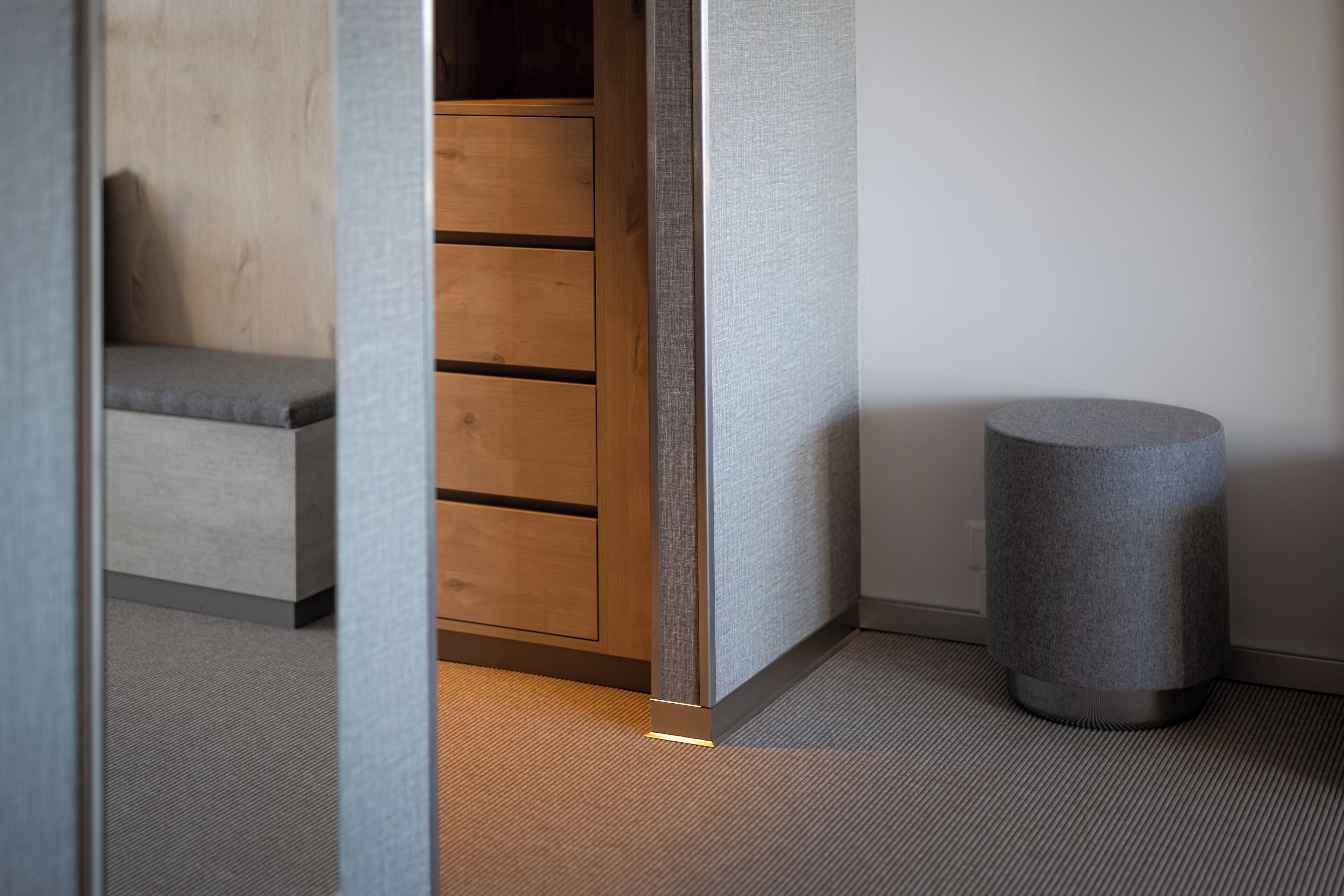 A modern room with a wooden cabinet, a grey textured wall, and a grey cylindrical object on the floor.