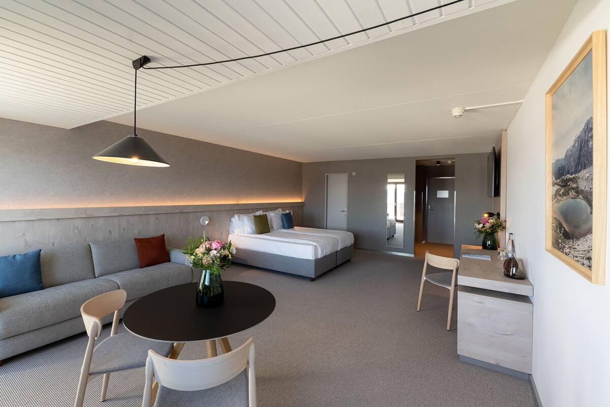 A modern hotel room with a sofa, a dining table, a bed, and a painting on the wall.