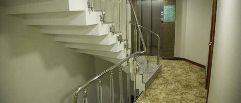 A carpeted staircase with metal railings leading to an elevator.
