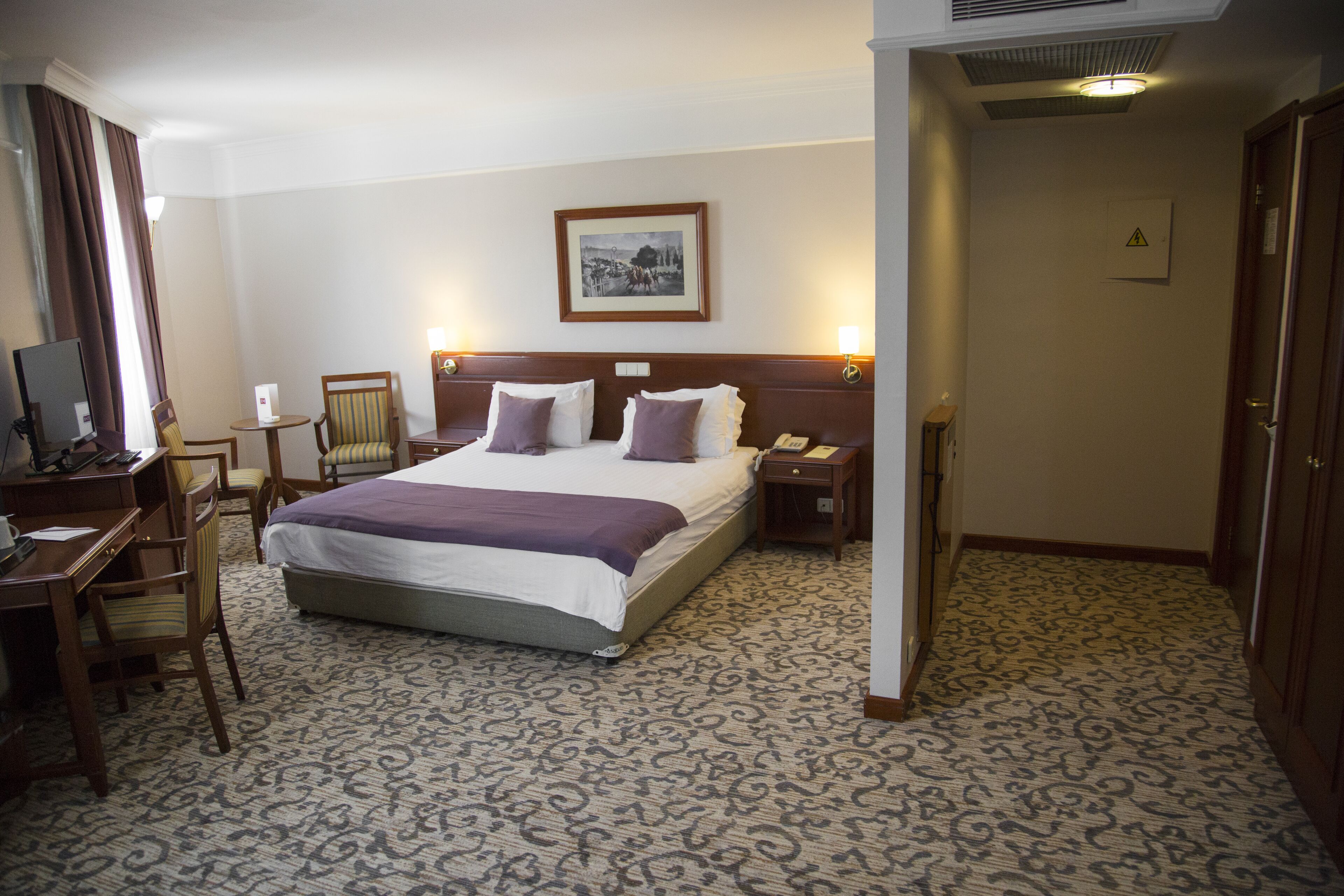Une chambre d’hôtel avec un grand lit, un bureau avec une chaise, une petite table et un téléviseur.