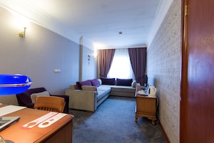 A hotel room with a sofa, chairs, a desk, a lamp, and a window with curtains.