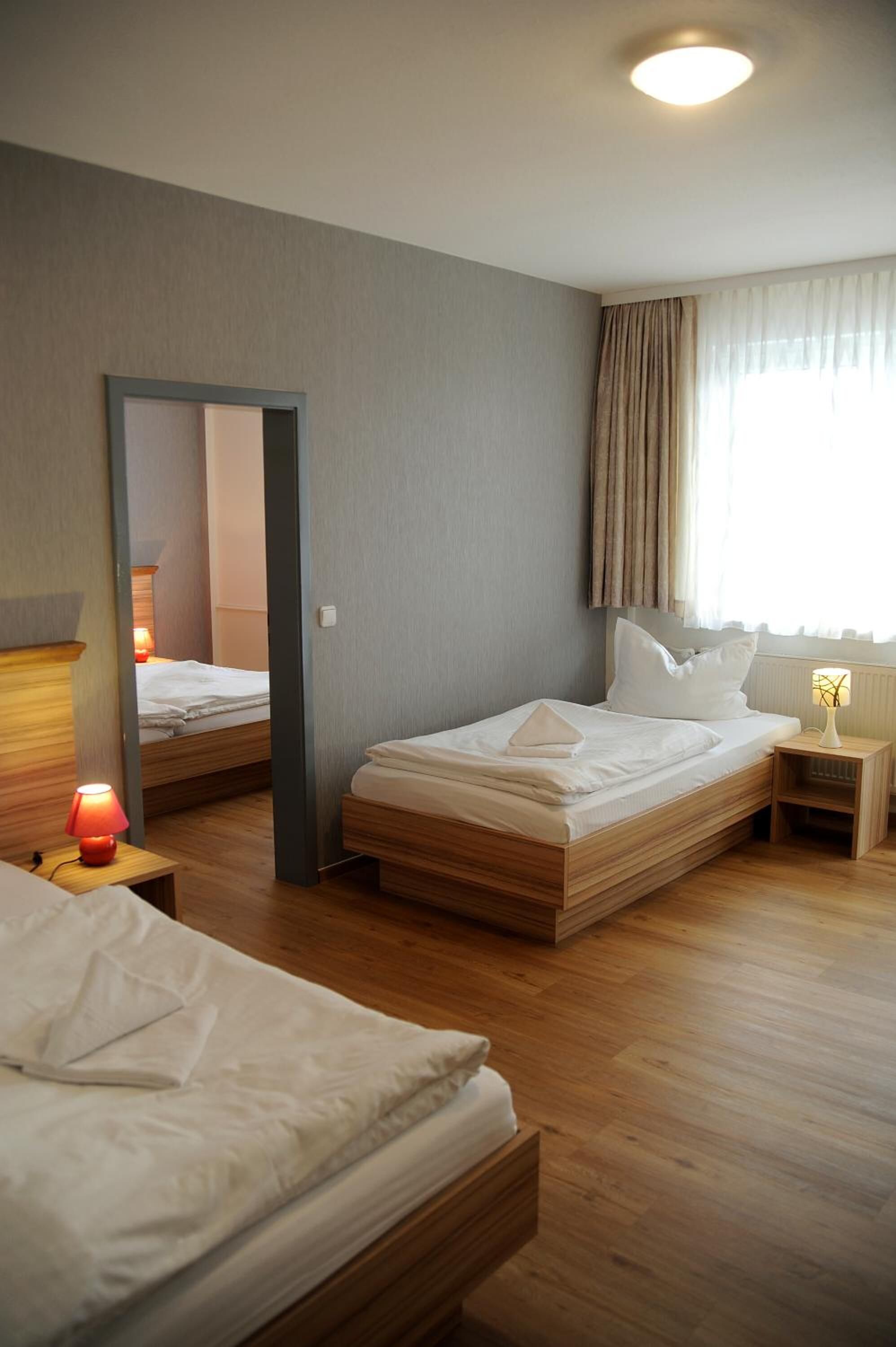 Et hotelværelse med to senge, et natbord med lampe, et spejl og et vindue med gardiner.
