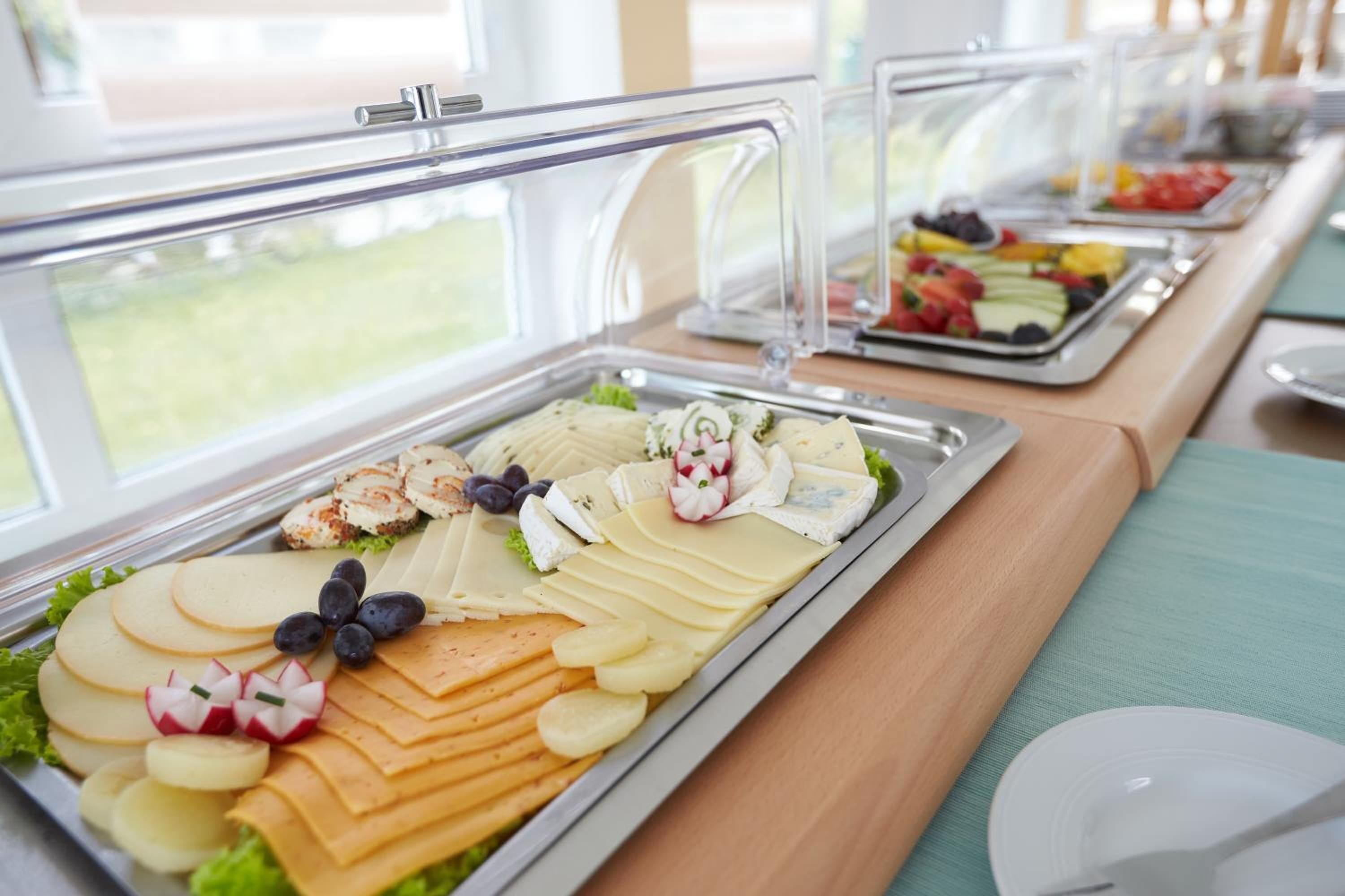 A buffet with various cheeses, fruits, and vegetables.