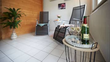 Une petite pièce accueillante, avec un sol carrelé, un mur en bois, une table surmontée d’un plateau en verre, une bouteille de vin et une chaise.