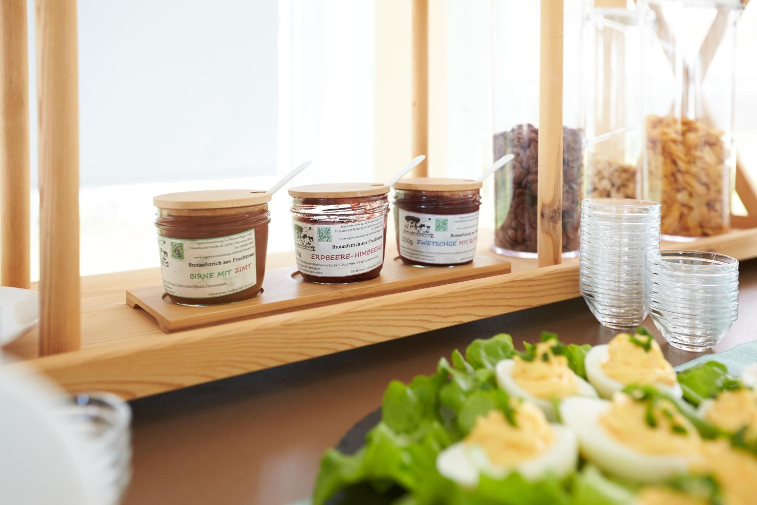 A buffet table with various food items including jars of spreads, a pitcher, and glasses of water.
