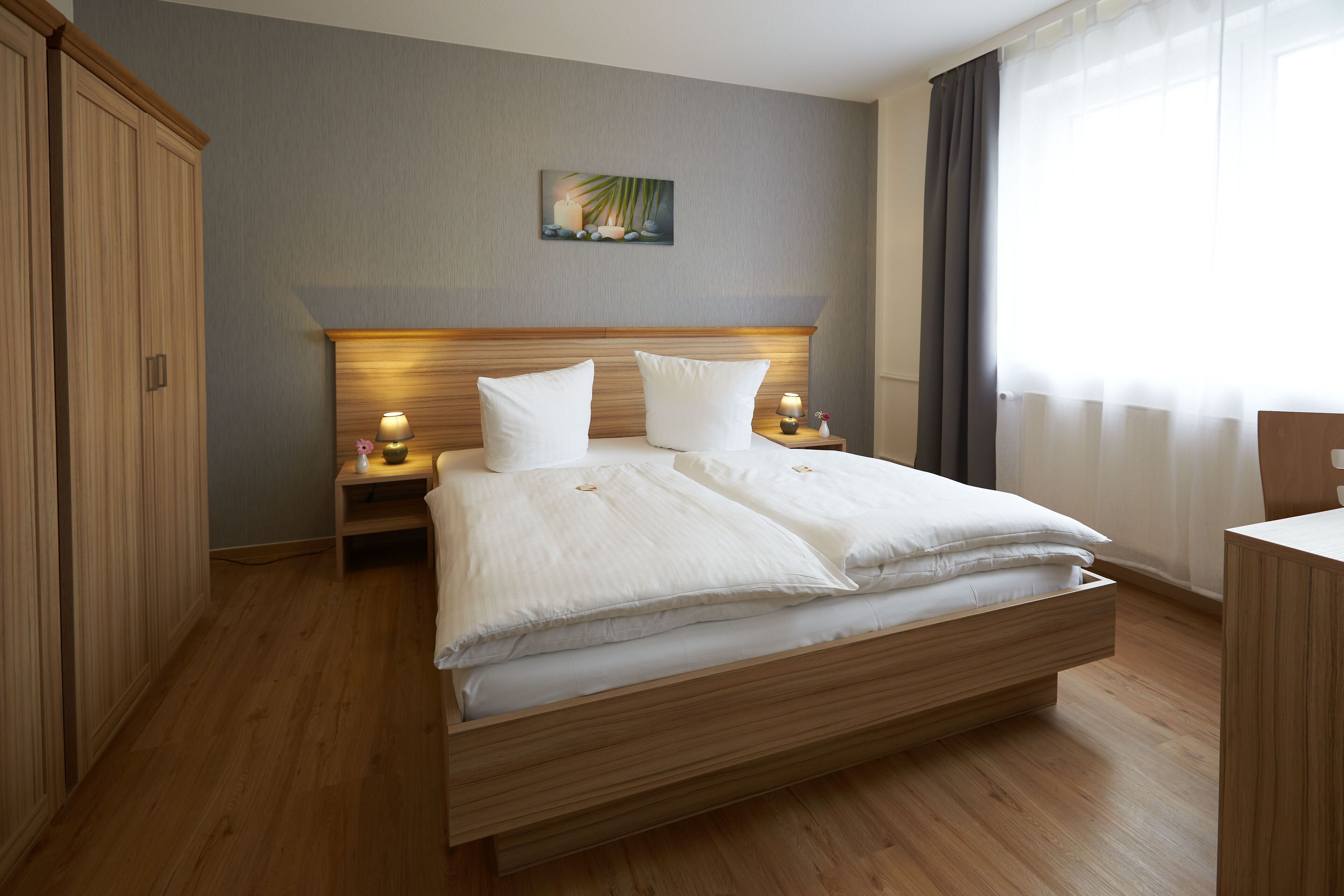 A modern hotel room with a wooden bed, a nightstand with a lamp, and a painting on the wall.