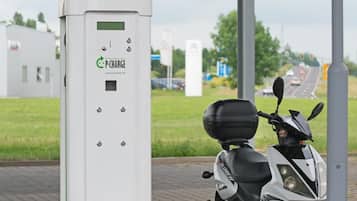 En P-charge el-scooterladestation med en hvid scooter parkeret i nærheden.