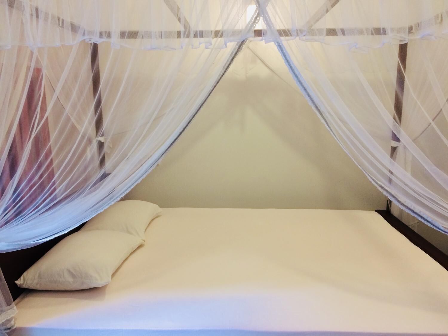 A single bed with a white mattress and pillows, covered by a white mosquito net.