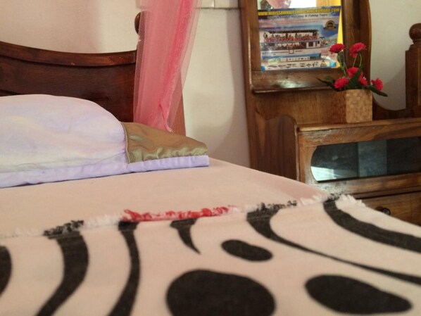 A bed with a pink canopy, a wooden nightstand with a vase of red flowers, and a mirror reflecting a poster. - Sun Rest Mirissa (Mirissa)