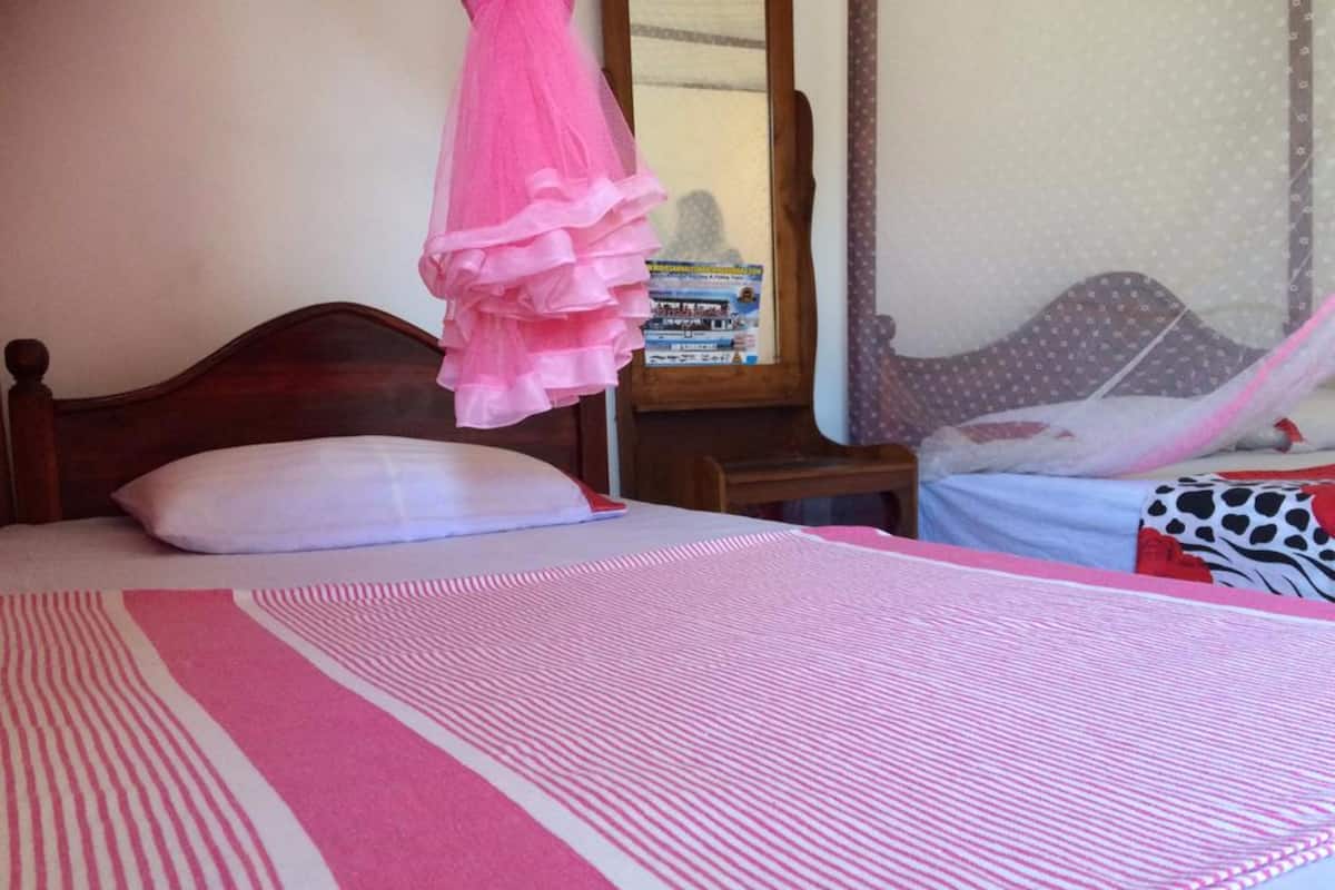 A bed with a striped bedspread, a wooden headboard, a bedside table with books, and a curtain.