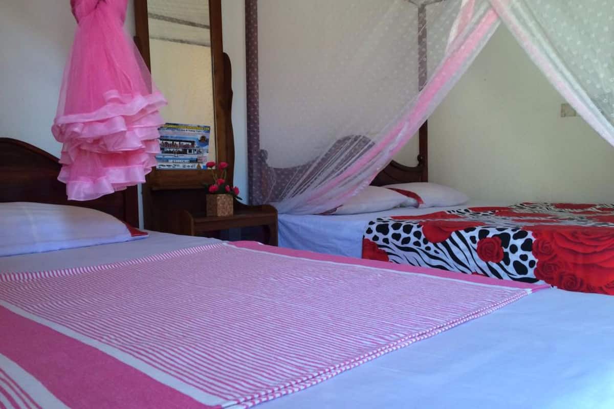 A bedroom with two beds, a wooden nightstand, a pink curtain, and a mosquito net.