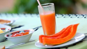 Et glas appelsinjuice med sugerør på et bord med et grønt borddække.