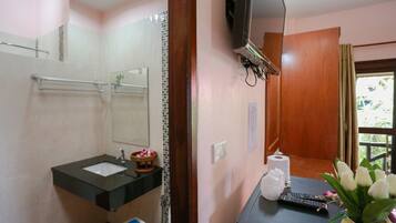 Un baño con lavamanos, espejo y televisor montado en la pared.