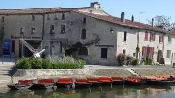 A historic stone building with a tiled roof, a fountain, and several boats docked in the water in front.