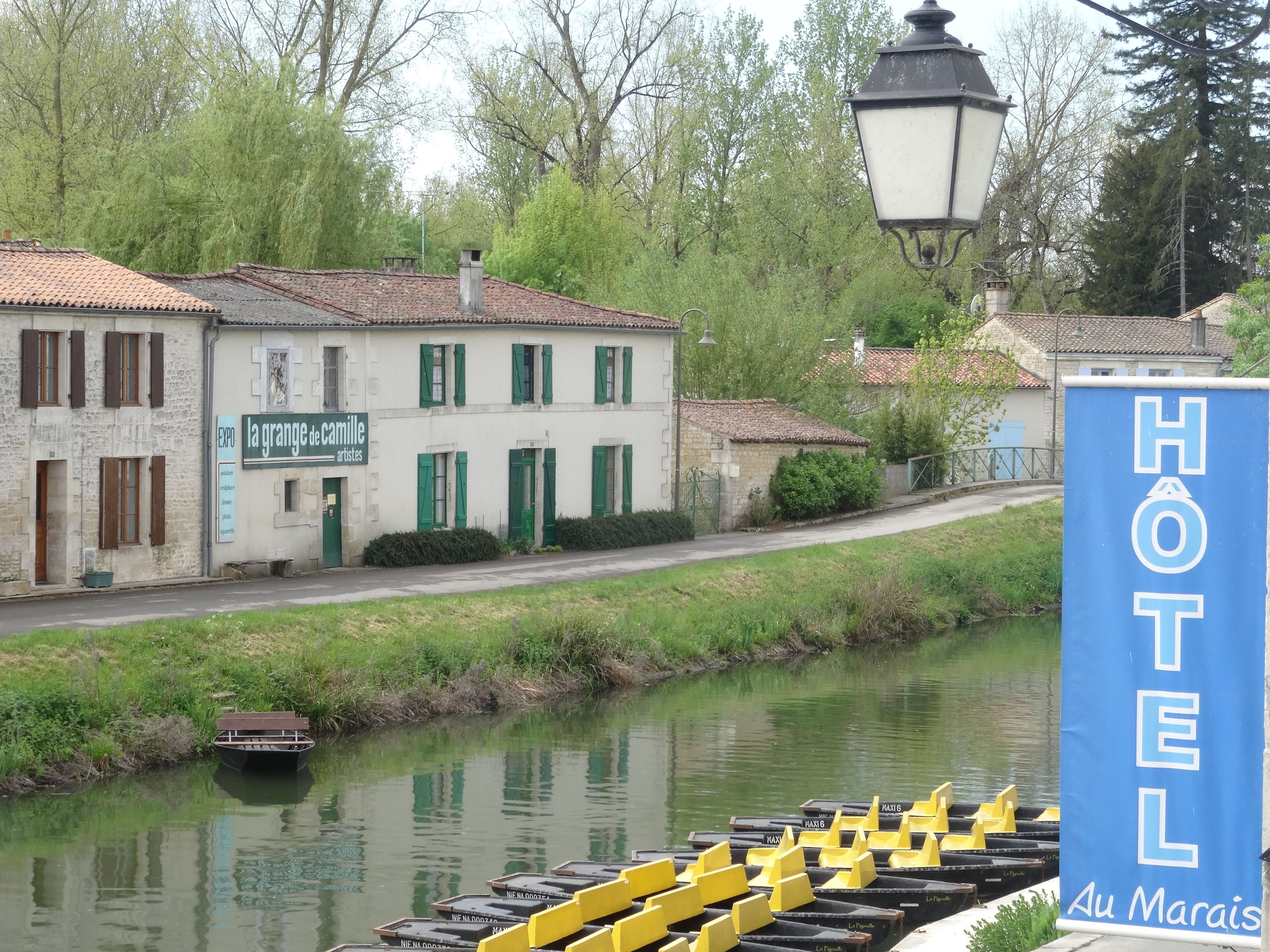 A hotel sign with "HOTEL Au Marais" and a row of yellow boats on a calm river.