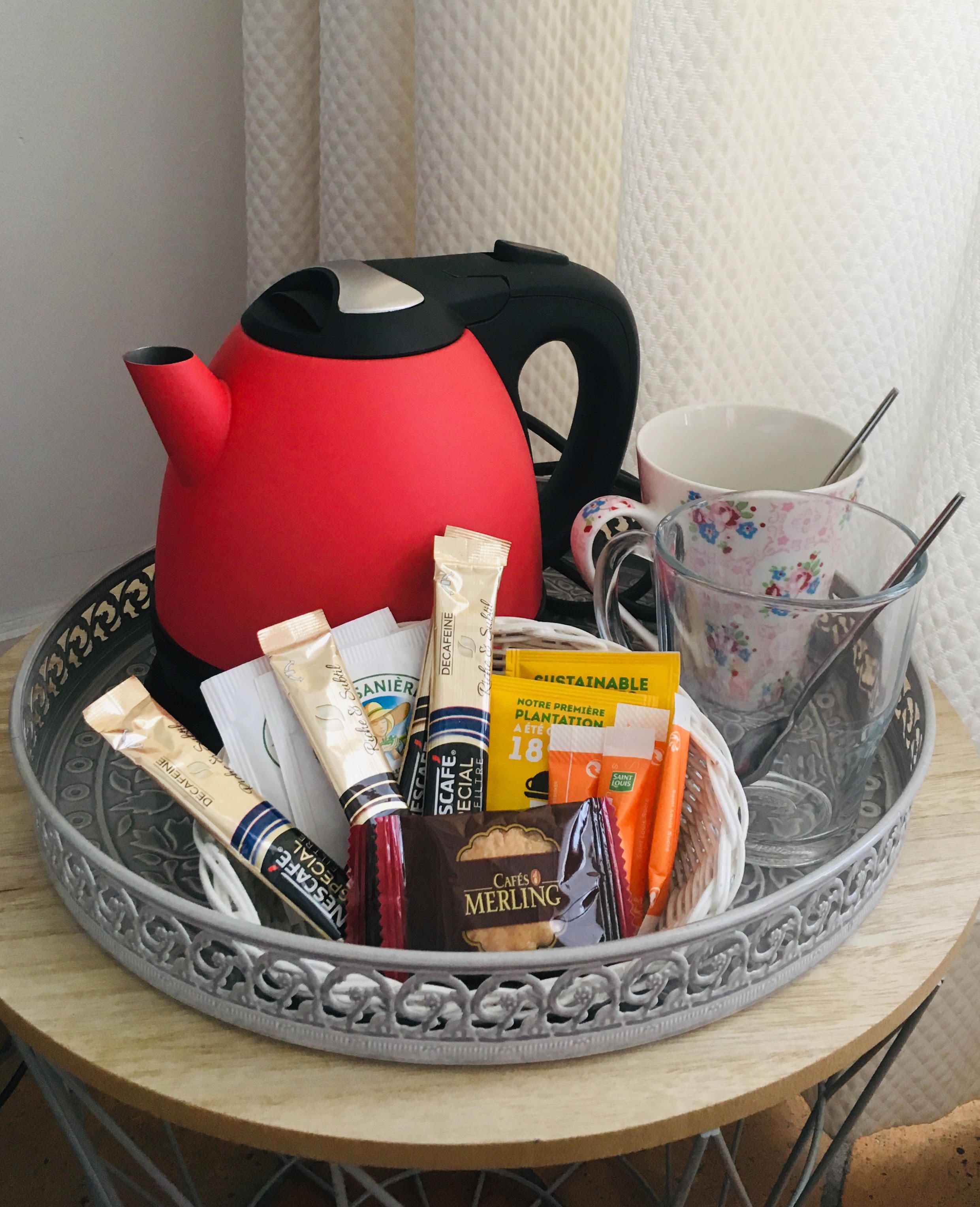 A tray with a red teapot, a floral mug, and various food items including chocolate and snacks.